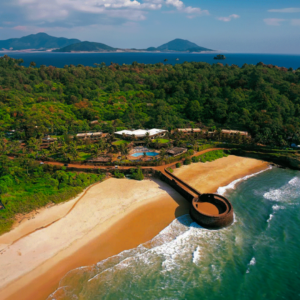 A scenic view of Sinquerim Beach in Goa featuring a large wooden bridge over a tranquil body of water.