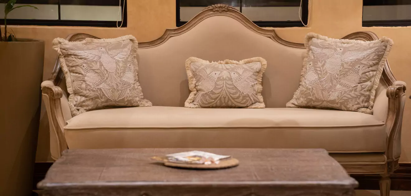 Elegant classic sofa with beige upholstery and two decorative pillows, against a wood-paneled backdrop. A wooden coffee table with a book sits in front.