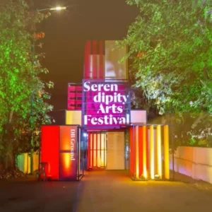 Illuminated entrance to "Serendipity Arts Festival" with colorful stacked containers at night.