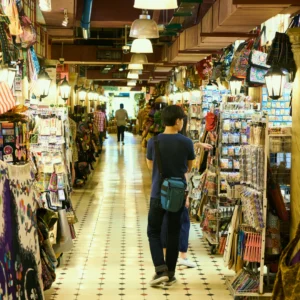 A person browsing at a stall in a vibrant indoor market aisle.