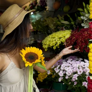 Woman in a straw hat holding a sunflower at a flower shop.