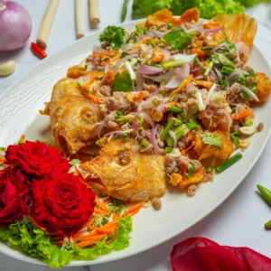 Plated spicy Thai salad with fried fish and garnishes on a white background.